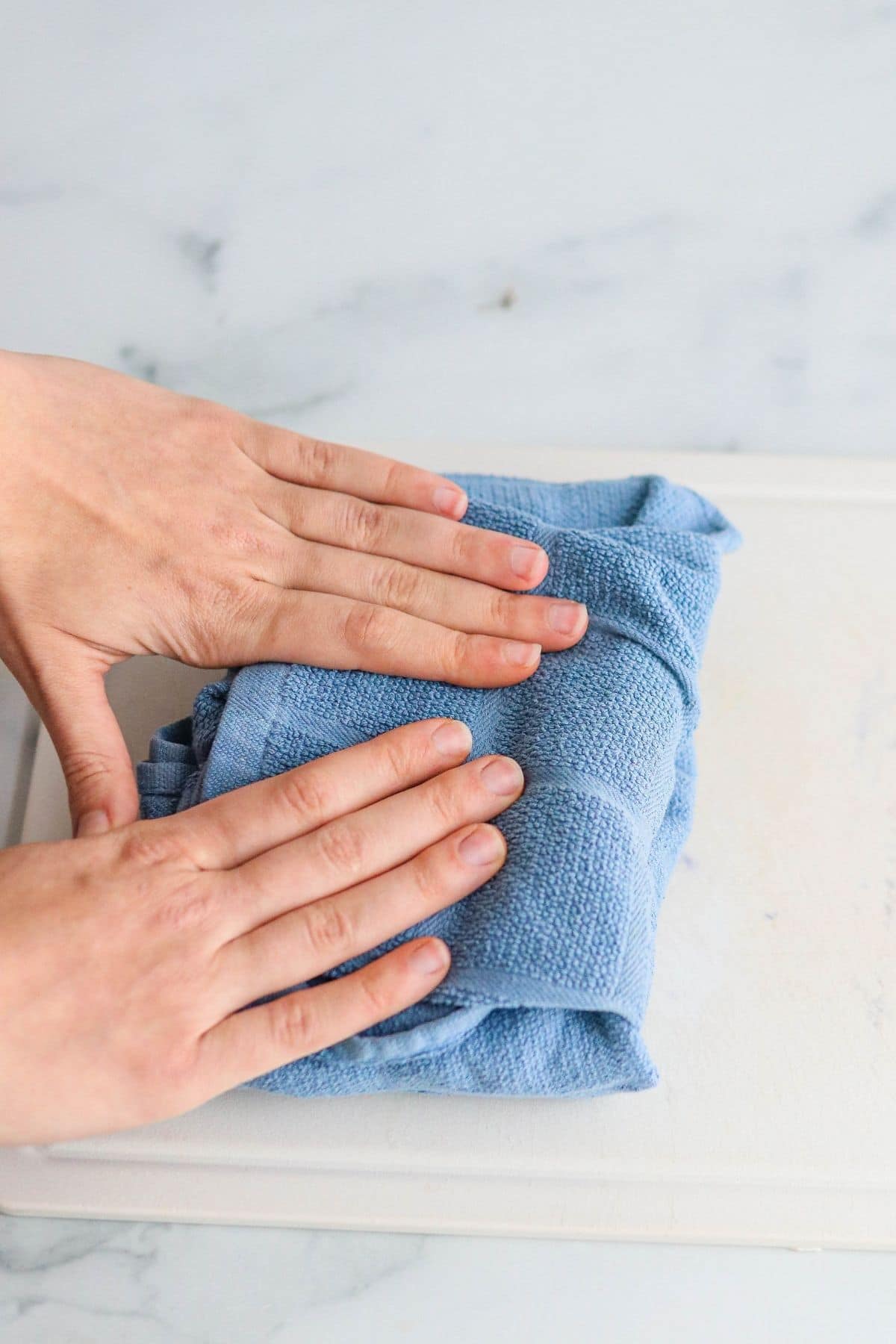 hands folding a blue towel over tofu to press.