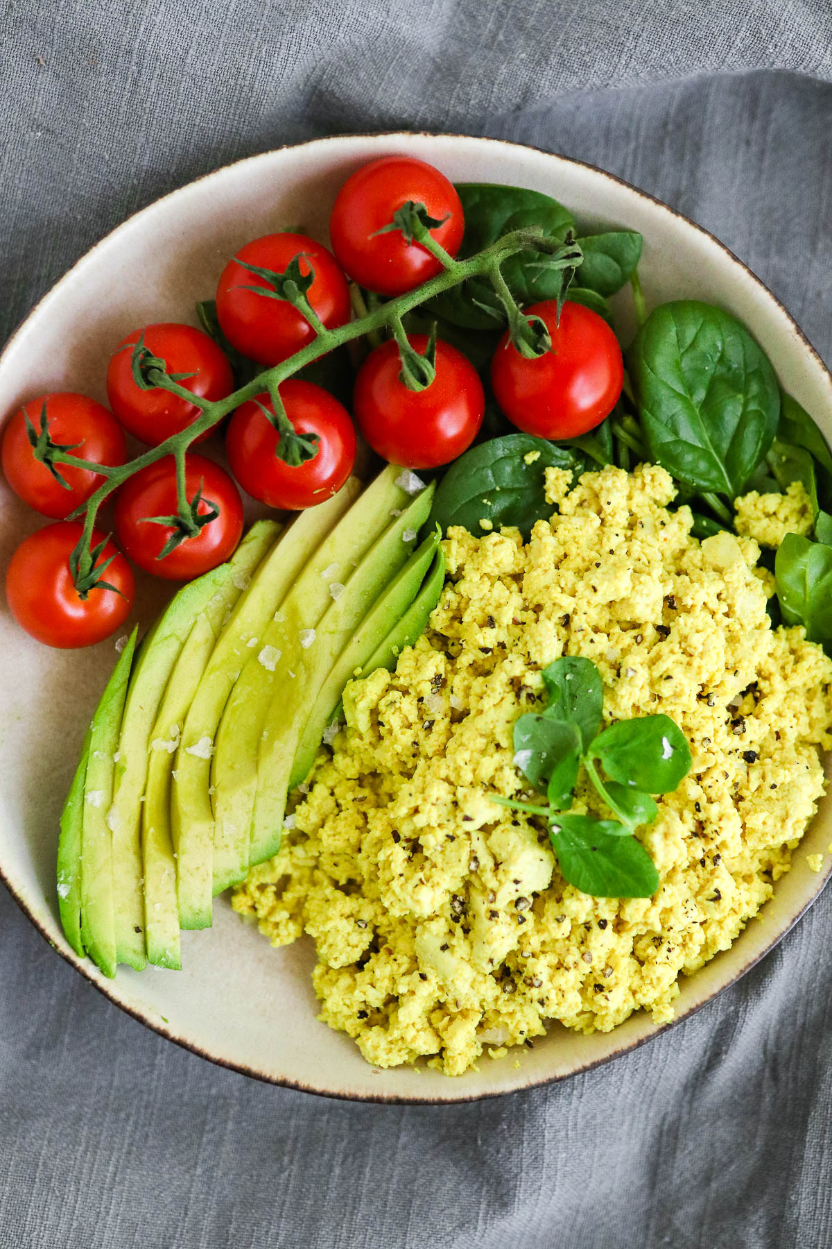 Vegan Tofu Scrambled Eggs on a plate with spinach, avocado, and tomatoes. 