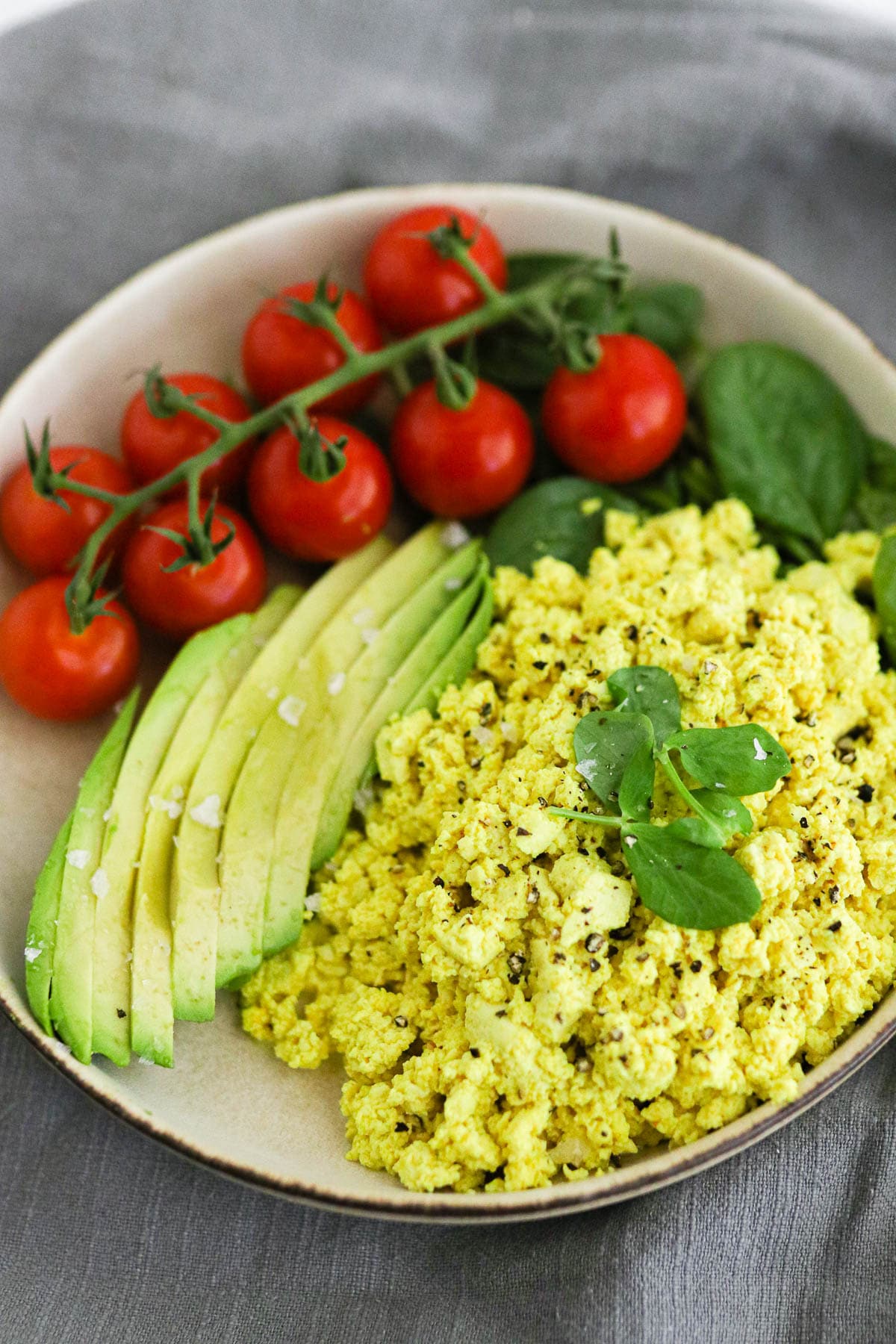 Vegan Tofu Scrambled Eggs on a plate with spinach, avocado, and tomatoes. 