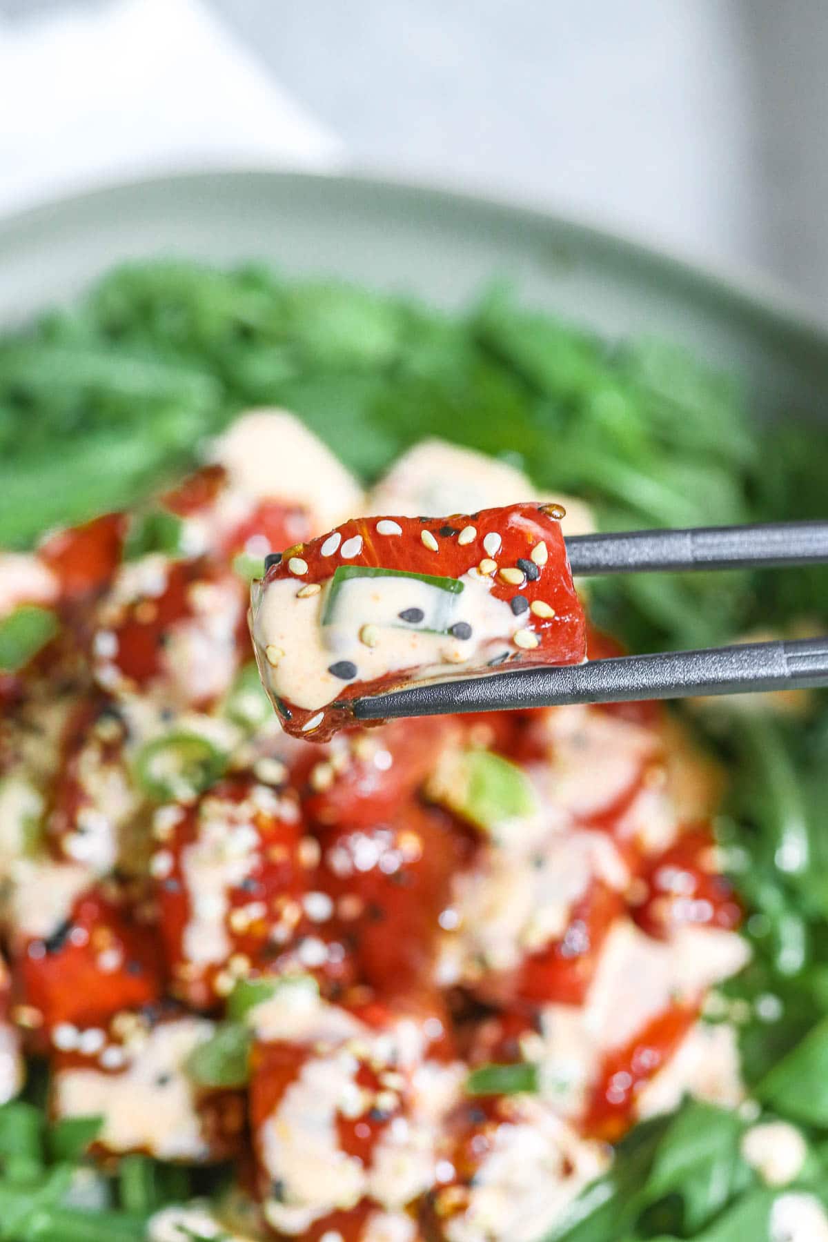 watermelon tuna with sauce being held by black chopsticks.