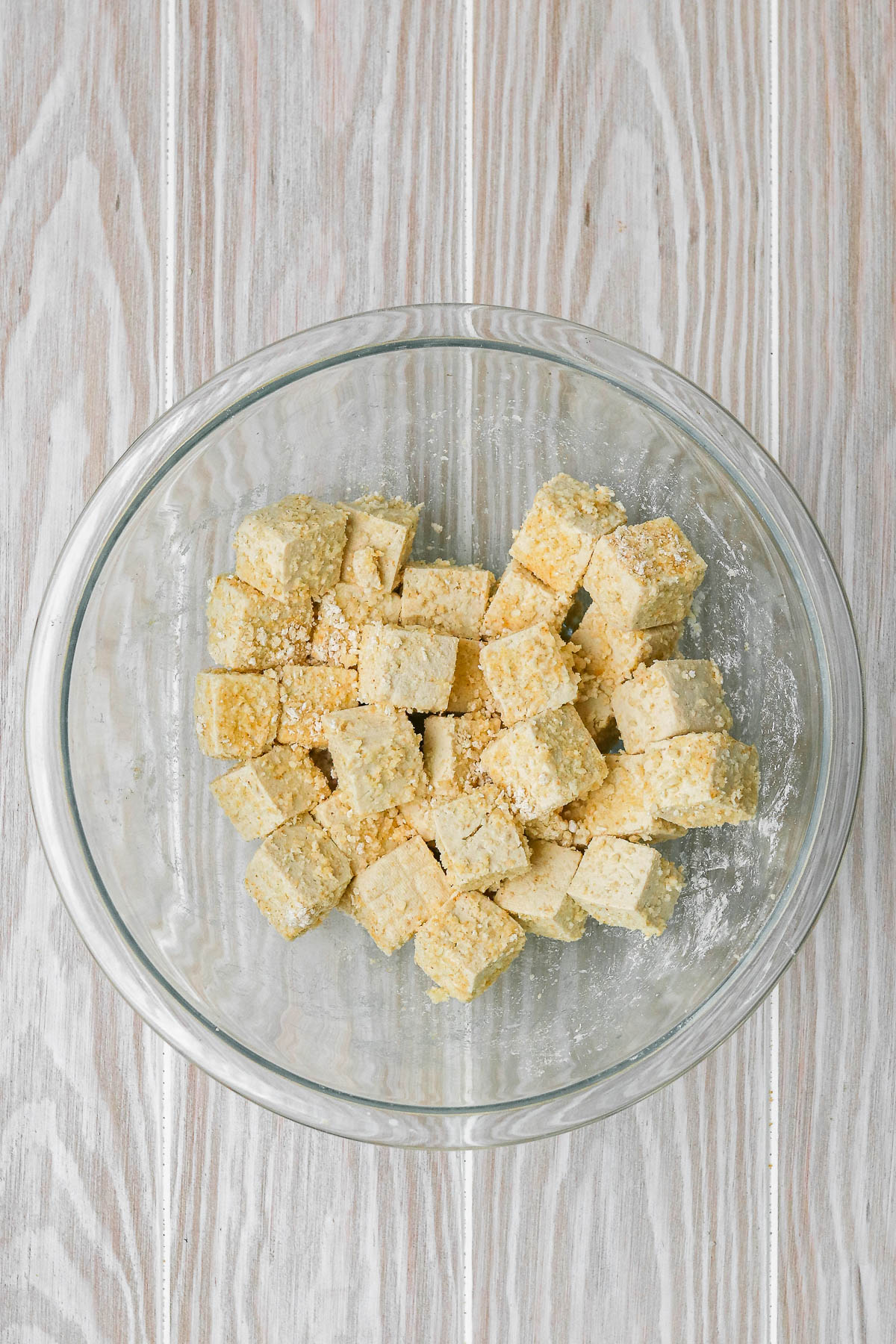 tofu cubes coated in dry mix in a clear bowl.