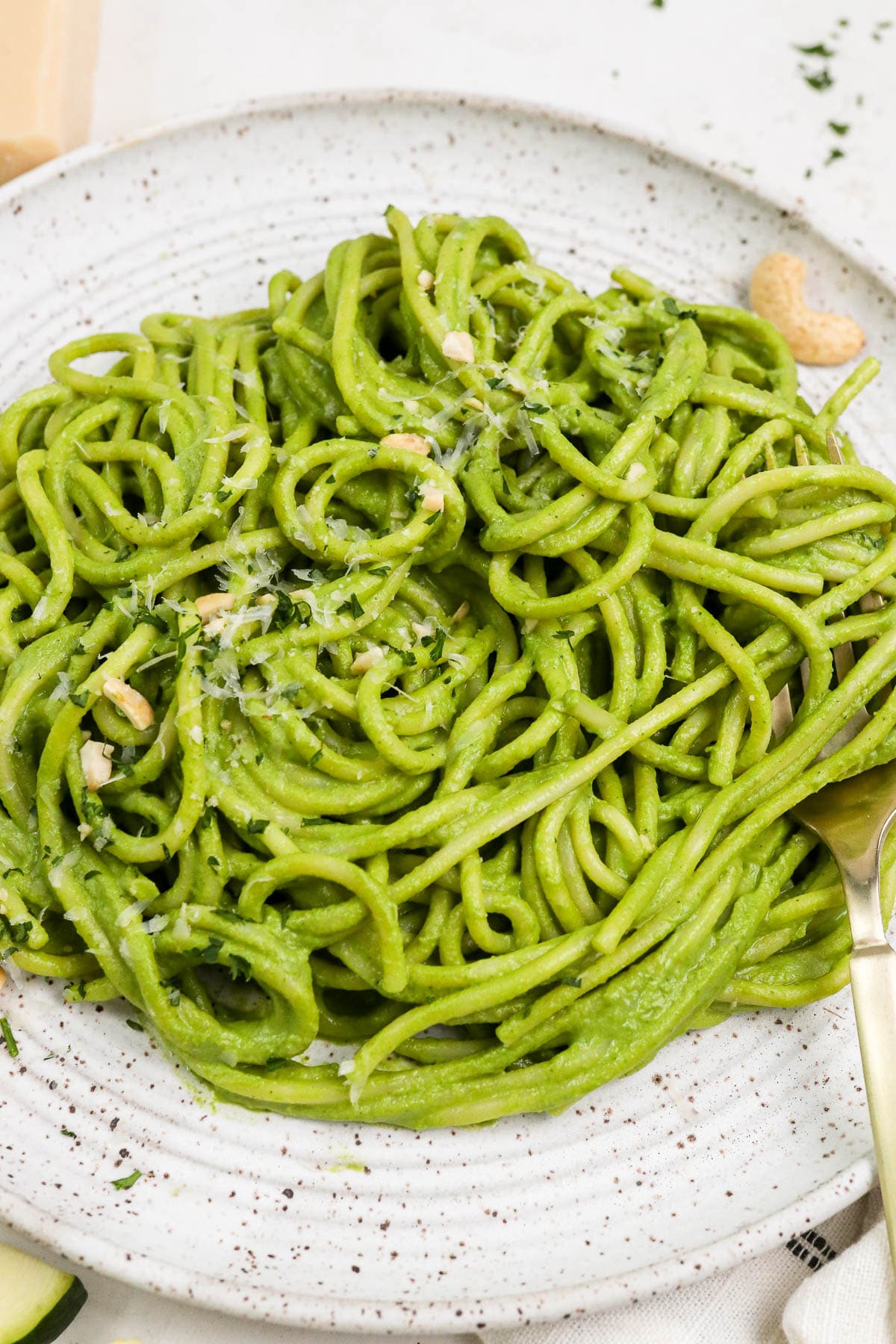 green pasta on a white plate with a fork twirling spaghetti.