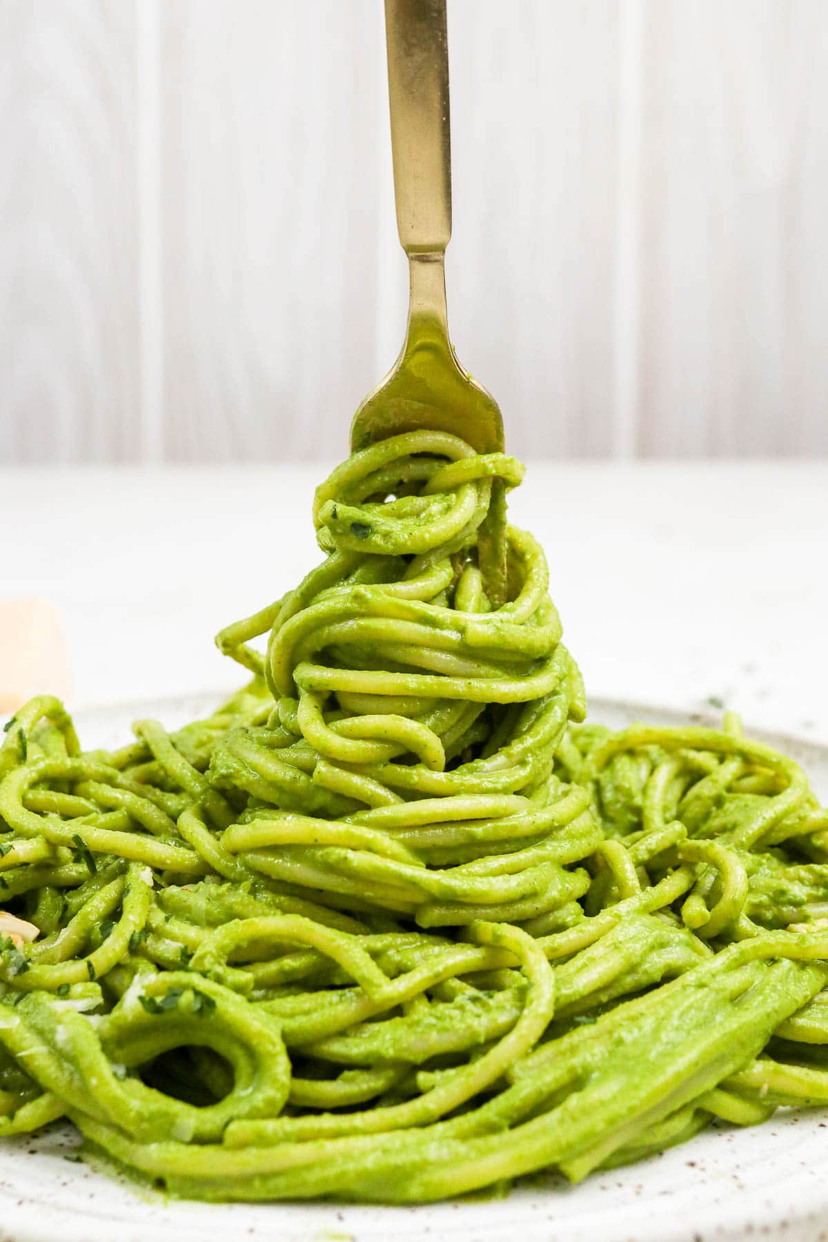 fork twirling green pasta upwards on a white plate.