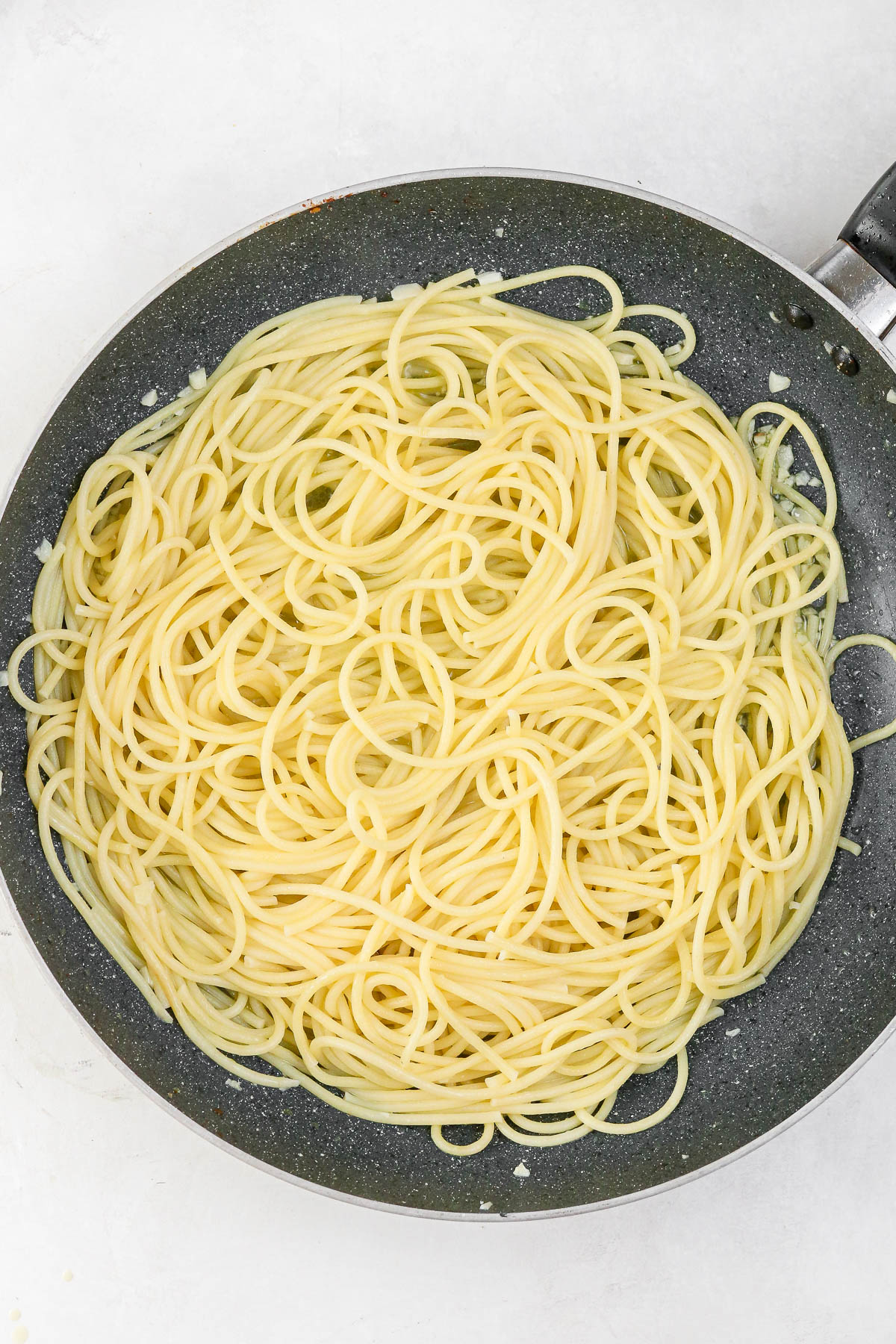 spaghetti in a pan tossed with garlic and oil.