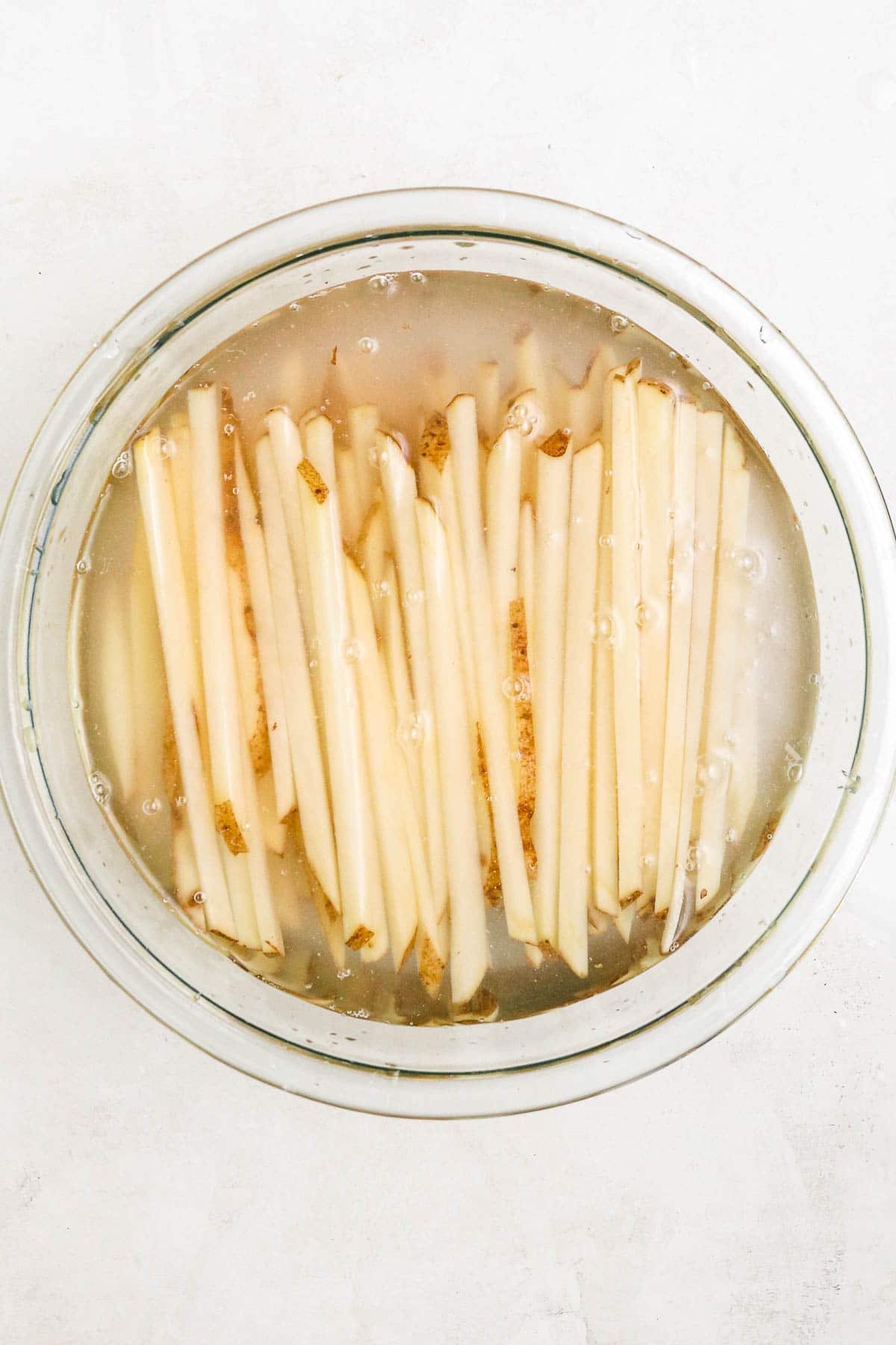 uncooked fries in a clear bowl full of water.
