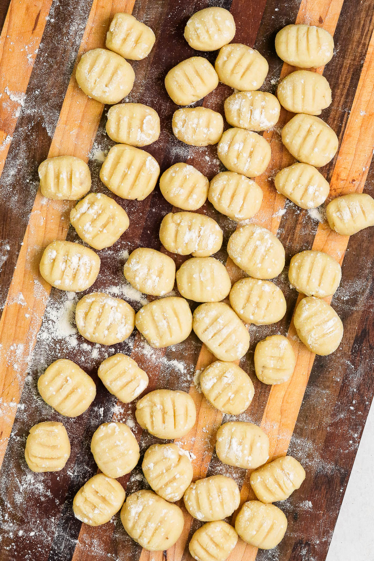 uncooked vegan gnocchi spread out on a brown wood cutting board.