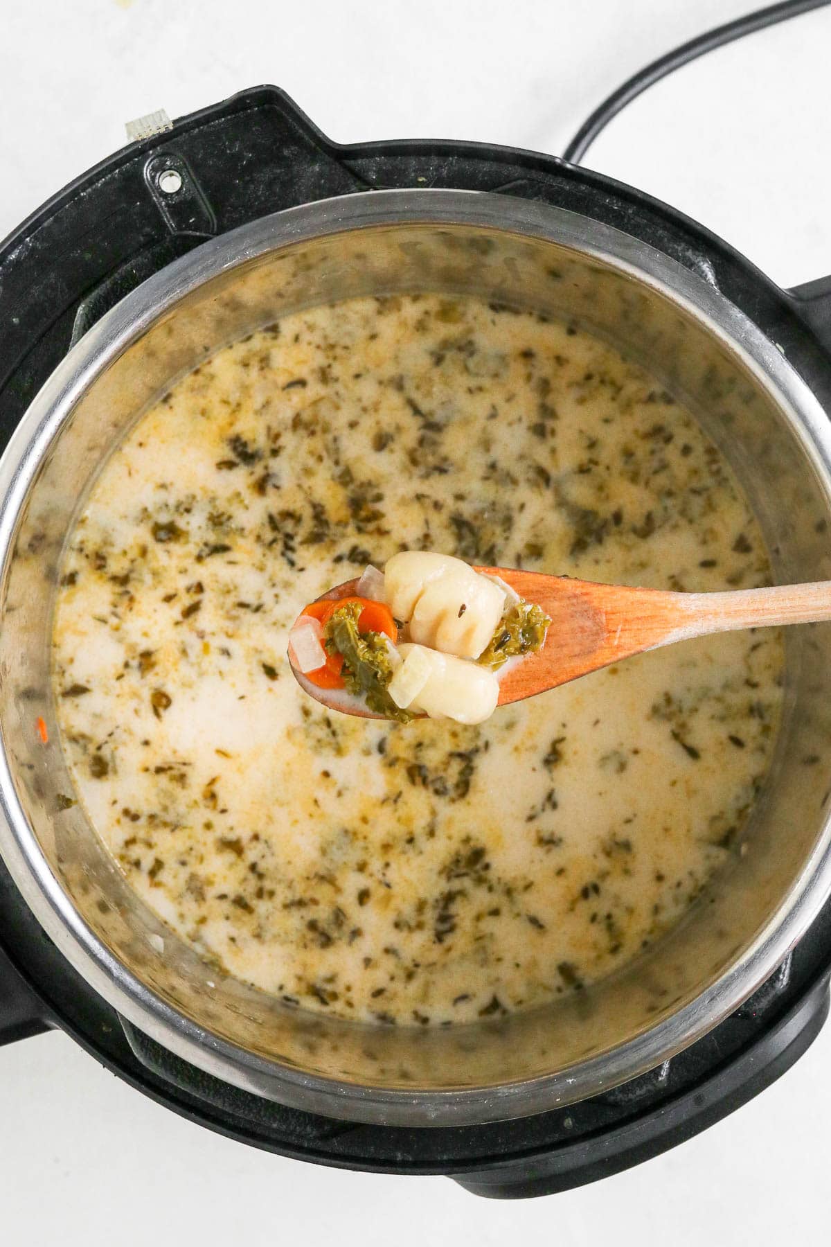 finished soup in the instant pot with wooden spoon holding gnocchi.