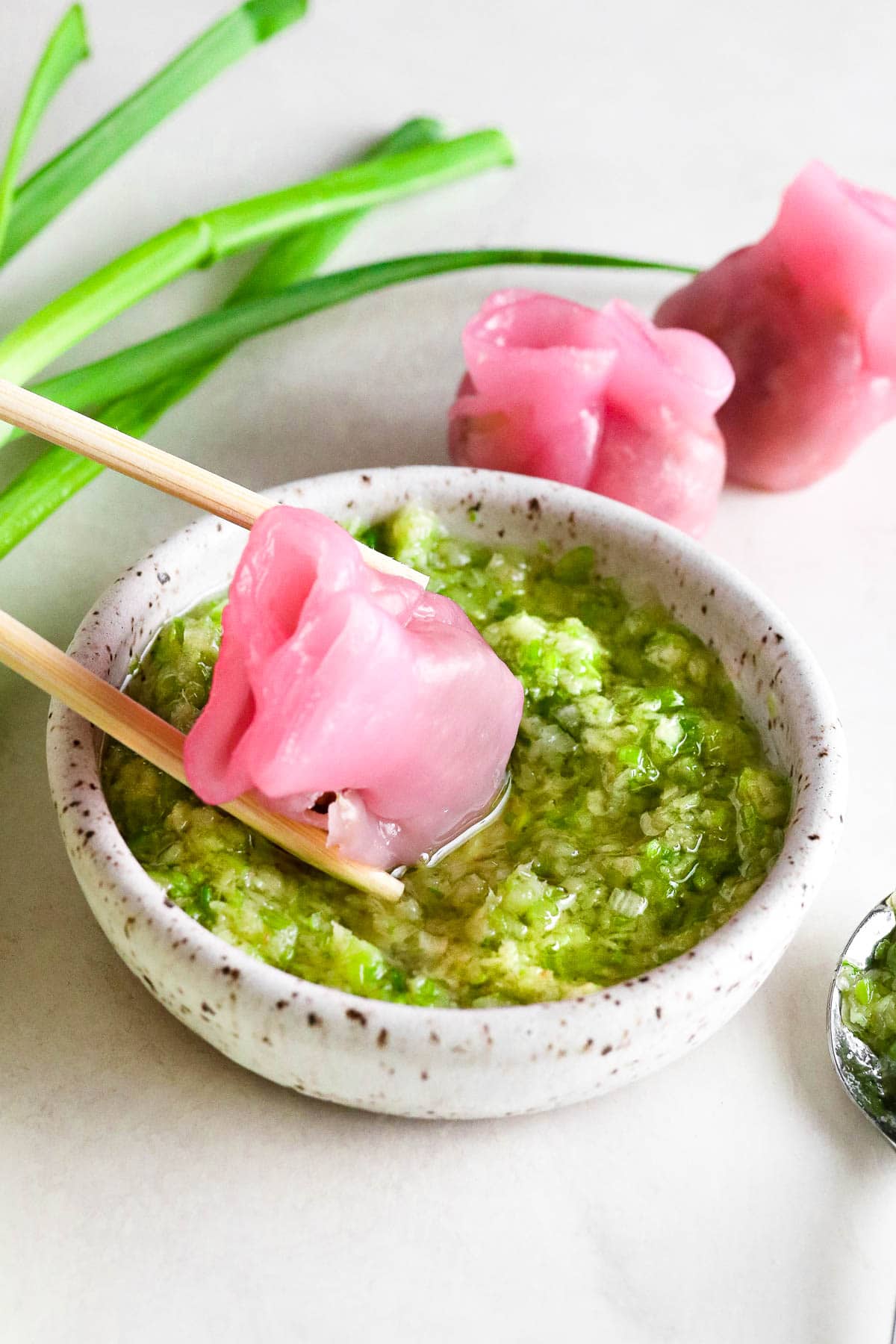 pink dumpling being dipped into ginger scallion sauce.