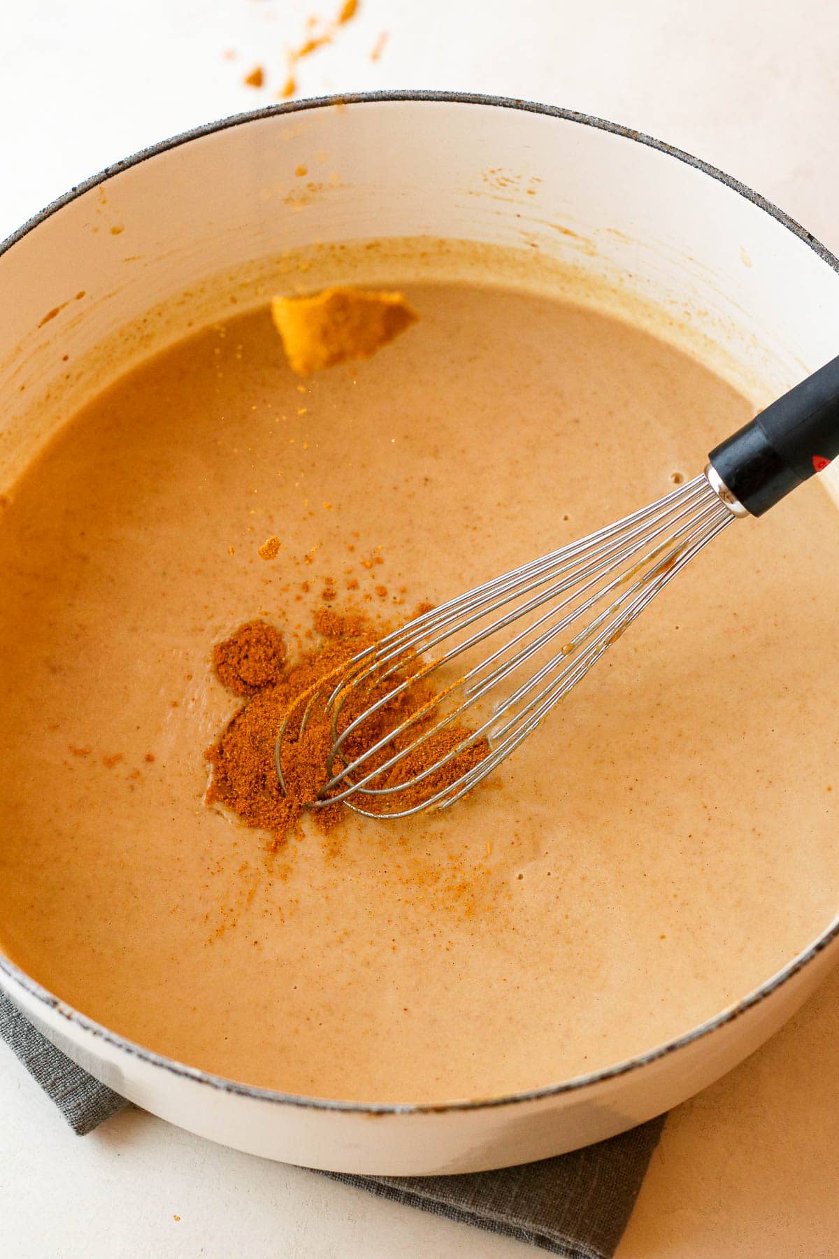 curry powder being added to sauce with whisk.