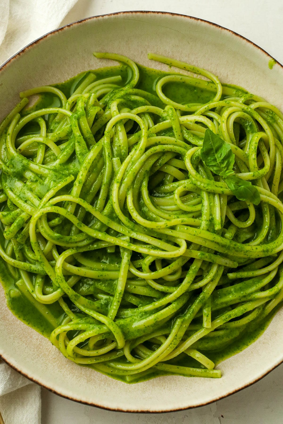 close up of green basil pasta in a white bowl.